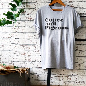 Puede incluir: Una camiseta gris con el texto "Coffee and Pigeons." impreso en negro.