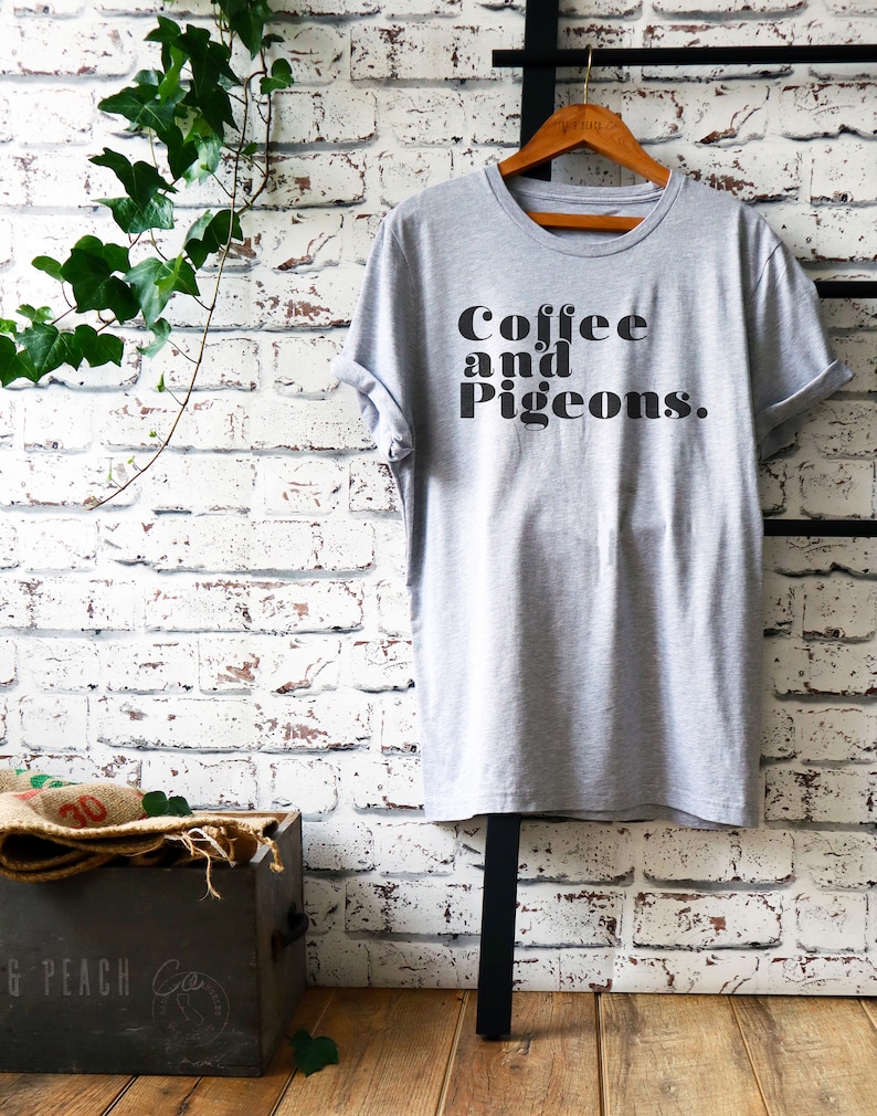 Puede incluir: Una camiseta gris con el texto "Coffee and Pigeons." impreso en negro.