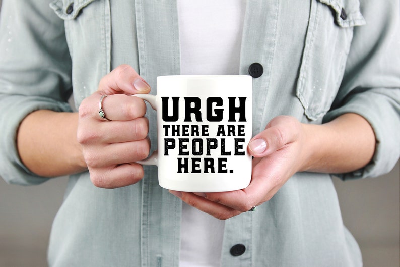 K&ouml;nnte beinhalten: Eine wei&szlig;e Keramik-Kaffeetasse mit schwarzem Text, der "URGH THERE ARE PEOPLE HERE." lautet.
