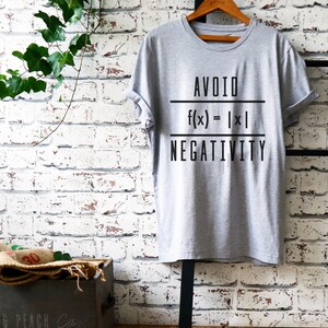 May include: Gray t-shirt with the text "AVOID" and a mathematical equation "f(x) = |x|" and the text "NEGATIVITY" printed on it.