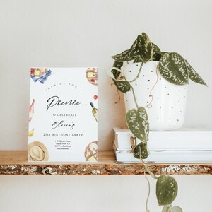 May include: A white card with a watercolor illustration of picnic food and a handwritten invitation to a picnic to celebrate Olivia's 21st birthday party. The invitation includes the date, time, location, and RSVP information.