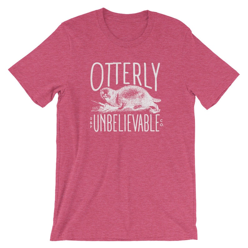 Puede incluir: Una camiseta rosa jaspeada con un gr&aacute;fico blanco de una nutria y el texto "OTTERLY UNBELIEVABLE CO."