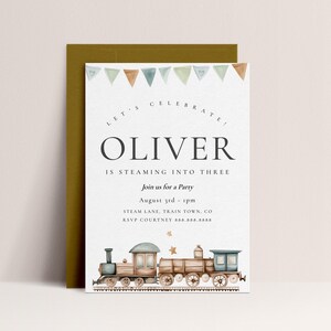 Puede incluir: Un tren azul y marrón con estrellas doradas en el lateral. El tren está sobre un fondo blanco con el texto "LET'S CELEBRATE! OLIVER IS STEAMING INTO THREE" y los detalles de la fiesta.