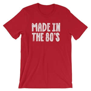 May include: Red short-sleeved t-shirt with white text that reads "MADE IN THE 80'S".