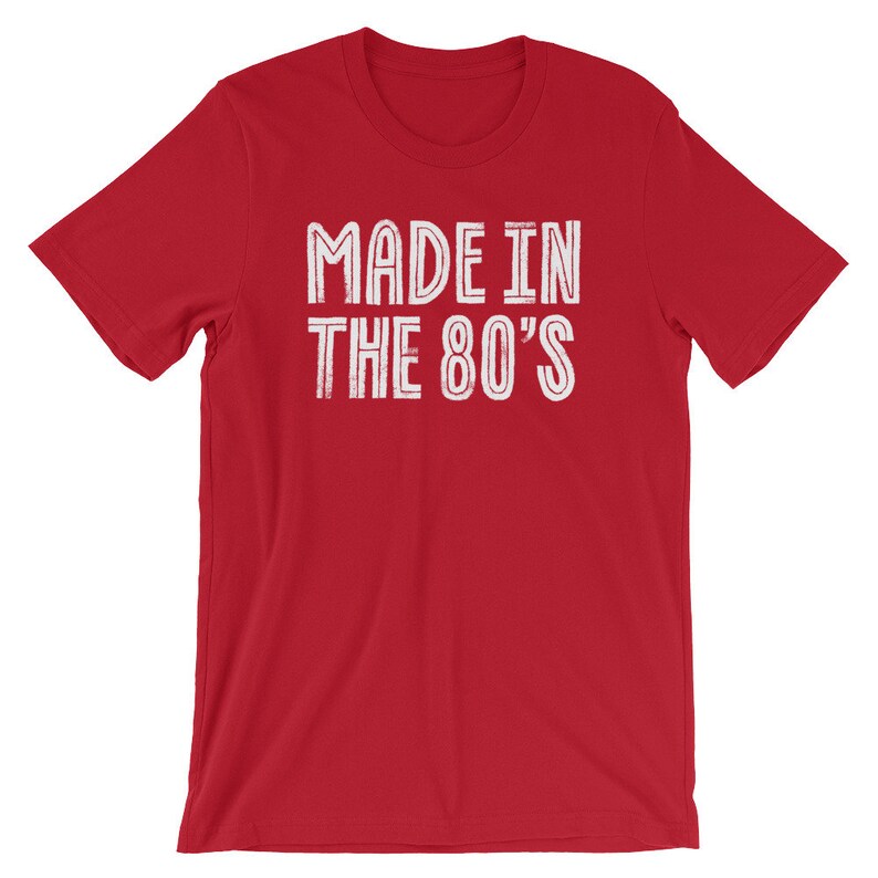 May include: Red short-sleeved t-shirt with white text that reads "MADE IN THE 80'S".