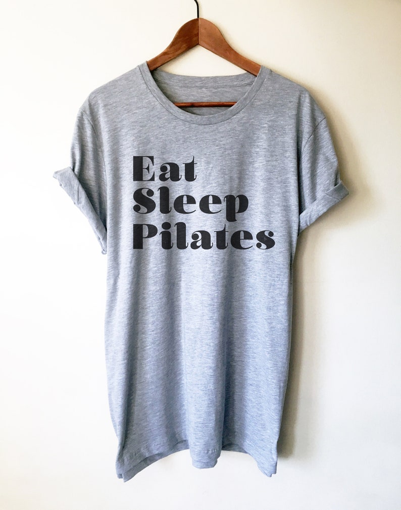 Pode incluir: Uma camiseta cinza mescla com o texto "Eat Sleep Pilates" impresso em preto.