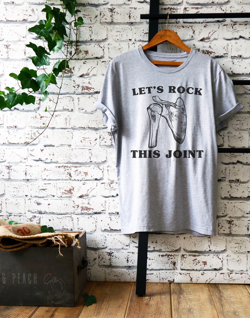 May include: Gray t-shirt with a black graphic of a shoulder joint and the text "Let's Rock This Joint".