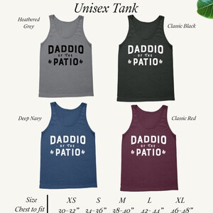 May include: Unisex tank top in five colors: heather grey, classic black, deep navy, classic red, and white. The tank top features the text "Daddio of the Patio" with a flame design on either side of the text. The tank top is available in sizes XS, S, M, L, and XL. Chest to fit measurements are provided for each size.