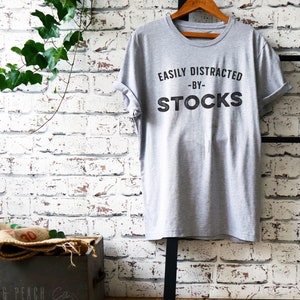 May include: Grey t-shirt with the text "Easily Distracted - By - Stocks" printed on the front.