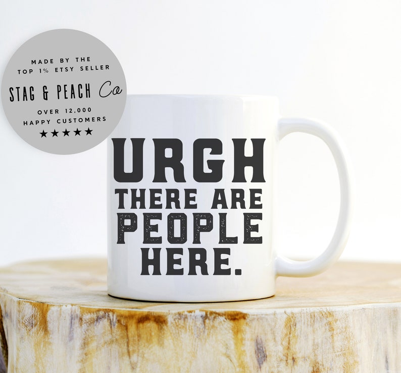 K&ouml;nnte beinhalten: Eine wei&szlig;e Keramik-Kaffeetasse mit schwarzem Text, der "URGH THERE ARE PEOPLE HERE." lautet.