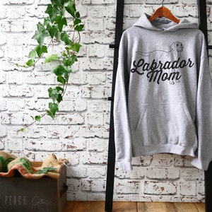 May include: Grey hooded sweatshirt with a black outline of a Labrador Retriever and the text "Labrador Mom" in a black cursive font.