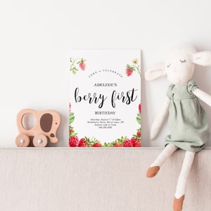 May include: A white invitation with a red and green strawberry border. The text reads "Come Celebrate Adeline's Berry First Birthday. Saturday August 7, 11-12pm, Strawberry Farm, Berry Lane, SD. Regrets only to Lana, 888.888.8888"