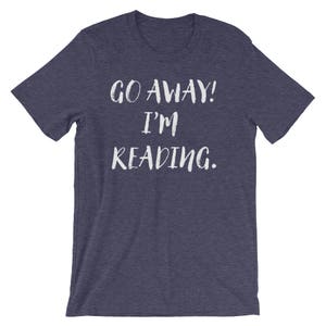 Puede incluir: Una camiseta azul marino con el texto "GO AWAY! I'M READING." en blanco.