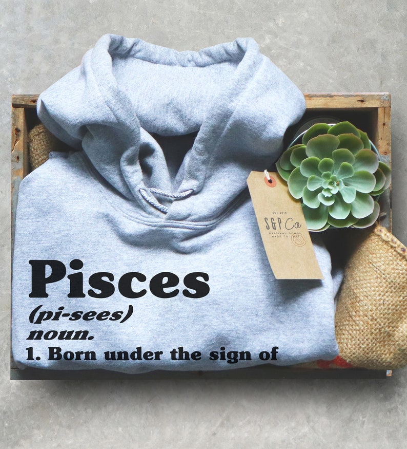 May include: A gray hooded sweatshirt with the word "Pisces" in black lettering, followed by the definition "(pi-sees) noun. 1. Born under the sign of".