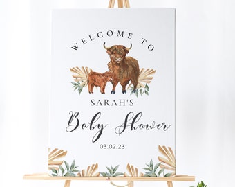 May include: Welcome to Sarah's Baby Shower sign featuring a watercolour illustration of a Highland cow and calf with tropical leaves. The date 03.02.23 is printed below the text.
