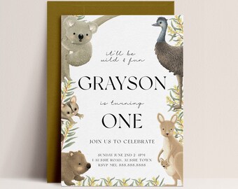 Puede incluir: Una tarjeta de invitación blanca con un borde verde que presenta varios animales australianos, incluyendo un koala, un wombat, un canguro y un emú. El texto en la tarjeta dice "It'll be wild & fun Grayson is turning one. Join us to celebrate Sunday June 2nd 2 pm 1 Aussie Road, Aussie Town RSVP Mel 888.888.8888"