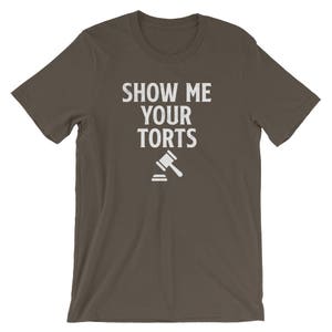 May include: A dark brown t-shirt with the text "Show Me Your Torts" in white lettering. A white gavel icon is below the text.