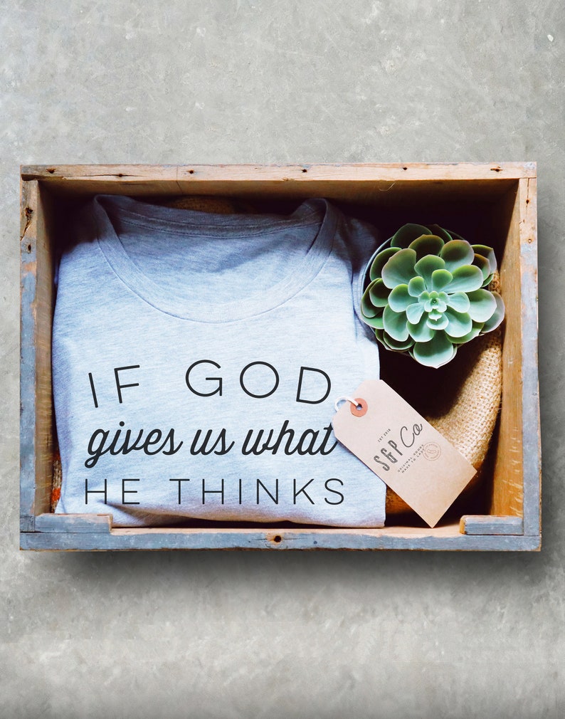 May include: A gray t-shirt with the text "If God gives us what He thinks" in black lettering. The t-shirt is in a wooden crate with a small green succulent plant and a brown tag with the text "SFF Co."