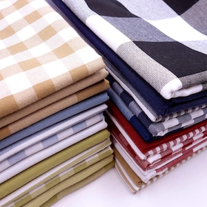 May include: A stack of folded checkered fabric in various colours, including tan, blue, green, red, and black. The fabric is folded neatly and arranged in a staggered pattern.