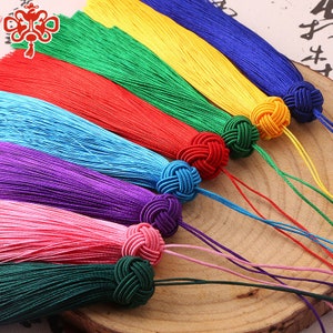 May include: A set of ten colorful tassel ornaments with knotted ends. The tassels are arranged in a rainbow pattern, with each tassel a different color: red, orange, yellow, green, blue, indigo, violet, pink, white, and black.