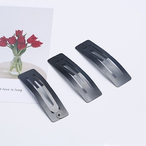 Könnte beinhalten: Drei schwarze Haarklammern aus Metall. Die Klammern sind rechteckig und leicht gebogen. Sie sind alle gleich groß.