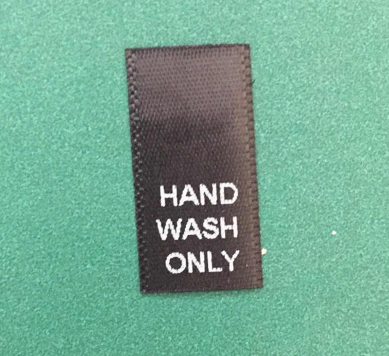 May include: Black fabric care label with white text that reads "HAND WASH ONLY".