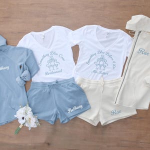 May include: Matching bridal party loungewear sets in light blue and cream colors. Includes hooded sweatshirts, shorts, and t-shirts with text: "Something Blue Crew Bridesmaid", "Something Blue Before I Do Mrs. Seibert", and names.