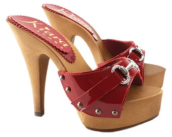Könnte beinhalten: Rote Lackplattform-Clogs mit einem Holzabsatz und einer silbernen Schnalle. Die Clogs sind mit silbernen Nieten besetzt und tragen den Markennamen "Kiana Shoes" auf dem Absatz.