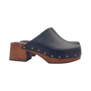 May include: Black leather clogs with a wooden platform and heel. The clogs have a rounded toe and are decorated with silver studs.