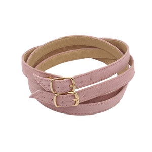 Könnte beinhalten: Ein Paar rosa Wildleder-Schuhriemen mit goldenen Schnallen. Die Riemen sind gefaltet und die Schnallen sind geschlossen.