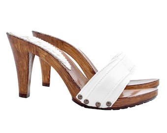 May include: White leather heeled clogs with a wooden platform and heel. The clogs have a single strap across the top of the foot and are secured with a buckle.