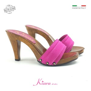 May include: A pair of pink suede heeled clogs with wooden soles and heels. The clogs have a strap across the top of the foot and are decorated with gold studs. The shoes are handmade in Italy.