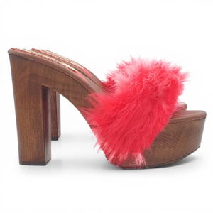 May include: Platform sandals with a wooden base and heel. The sandals feature a vibrant pink fluffy strap across the top. The wooden heel is approximately 4 inches high.