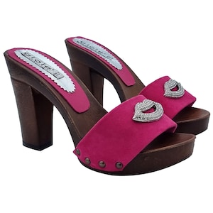 May include: A pair of pink suede heeled clogs with a wooden platform and a rhinestone lip design on the strap.