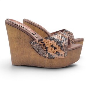 Peut inclure: Sandales compensées marron avec un motif peau de serpent sur les lanières. Les sandales ont une plateforme et un talon en bois, et sont fixées par de petits clous argentés. Chaussures pour une tenue décontractée.