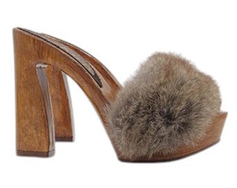May include: Brown wooden platform clogs with a thick fur pom-pom on the top of the shoe.