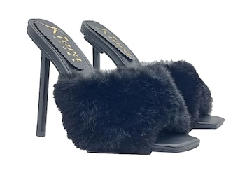 May include: Black faux fur heeled mules with a square toe and a thin stiletto heel. The heels have a gold logo that says "Kenza Styles".