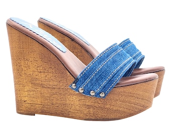 May include: A pair of brown wooden wedge sandals with blue denim straps and silver studs. The sandals have a closed toe and an open heel.