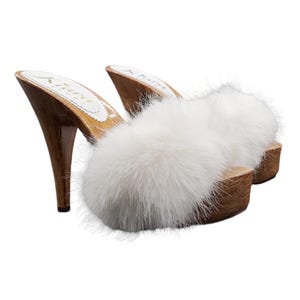 May include: A pair of white fur-trimmed wooden clogs with a high heel. The clogs are made of natural wood and have a soft, fluffy white fur trim around the top.