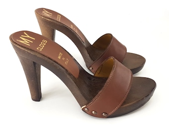 May include: Pair of brown leather heeled clogs with a wooden platform and heel. The clogs have a single strap across the top of the foot and are labeled "MY CLOGS" on the insole. The label also states "MADE IN ITALY".