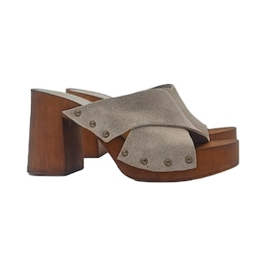 May include: Beige suede platform clogs with a wooden heel and a criss-cross strap design. The clogs have metal studs around the strap and heel.