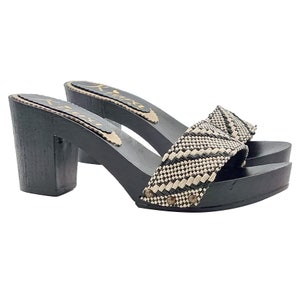May include: Black and white woven fabric clogs with a black wooden heel. The clogs have a geometric pattern and are accented with small metal studs.