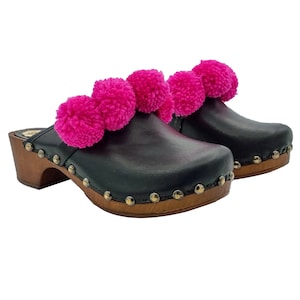 May include: Black leather clogs with a wooden platform sole and pink pom-poms around the top of the shoe.