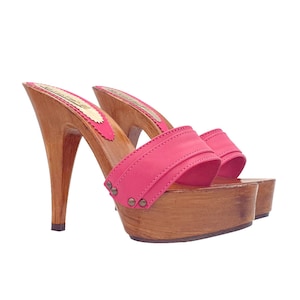 May include: A pair of pink wooden platform clogs with a high heel. The clogs have a single strap across the top of the foot and are decorated with small metal studs.