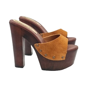 May include: A pair of brown suede platform clogs with a wooden heel and platform. The clogs have a brown suede upper with a pointed toe and a buckle closure. The heel is about 4 inches high and the platform is about 1 inch high.