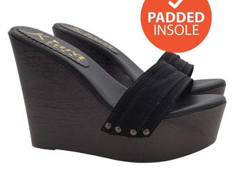 Könnte beinhalten: Schwarze Keilsandalen mit gepolsterter Innensohle und einem schwarzen Stoffband mit goldenen Akzenten. Die Sandalen haben einen Keil Absatz aus Holz.