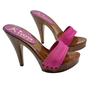 May include: A pair of pink wooden platform clogs with a high heel. The clogs have a pink fabric strap and are decorated with small silver studs.