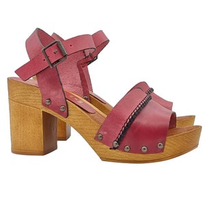 May include: Red leather heeled sandals with a wooden platform and black stitching detail. The sandals have a buckle closure and a peep toe.