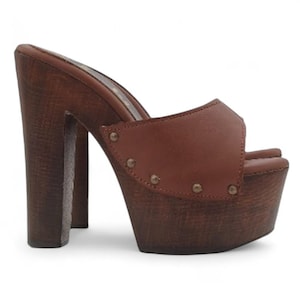 May include: Brown platform clogs with a wooden sole and heel. The open-toe shoe features a brown leather upper secured with small metal studs. The chunky heel and platform sole provide a bold, retro look.