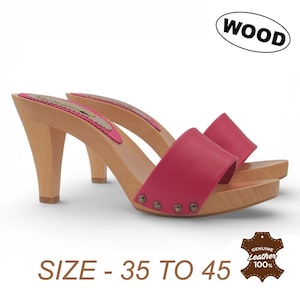 Könnte beinhalten: Ein Paar Holzclogs mit hohen Absätzen. Die Clogs haben einen leuchtend pinkfarbenen Lederriemen und eine Holzsohle. Die Absätze sind aus hellfarbenem Holz. Der Text "WOOD" befindet sich in einem weißen Oval.
